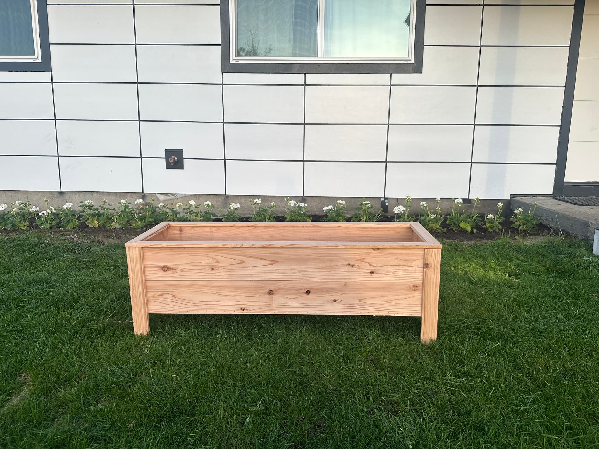 Long low-profile cedar raised bed with short legs, side view against house
